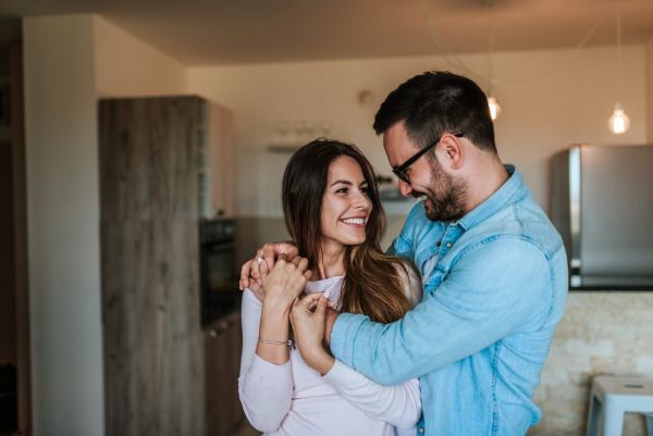 Happy man and woman couple hug each other inside of an apartment kitchen