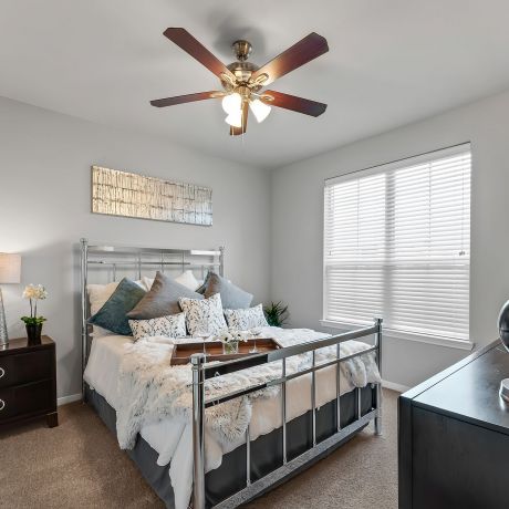 Gateway Cedars apartment bedroom with large windows, ceiling fan, and furnished with a bed and dresser